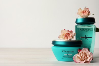 Photo of MYKOLAIV, UKRAINE - SEPTEMBER 07, 2021: Kerastase hair care cosmetic products and beautiful flowers on white wooden table. Space for text