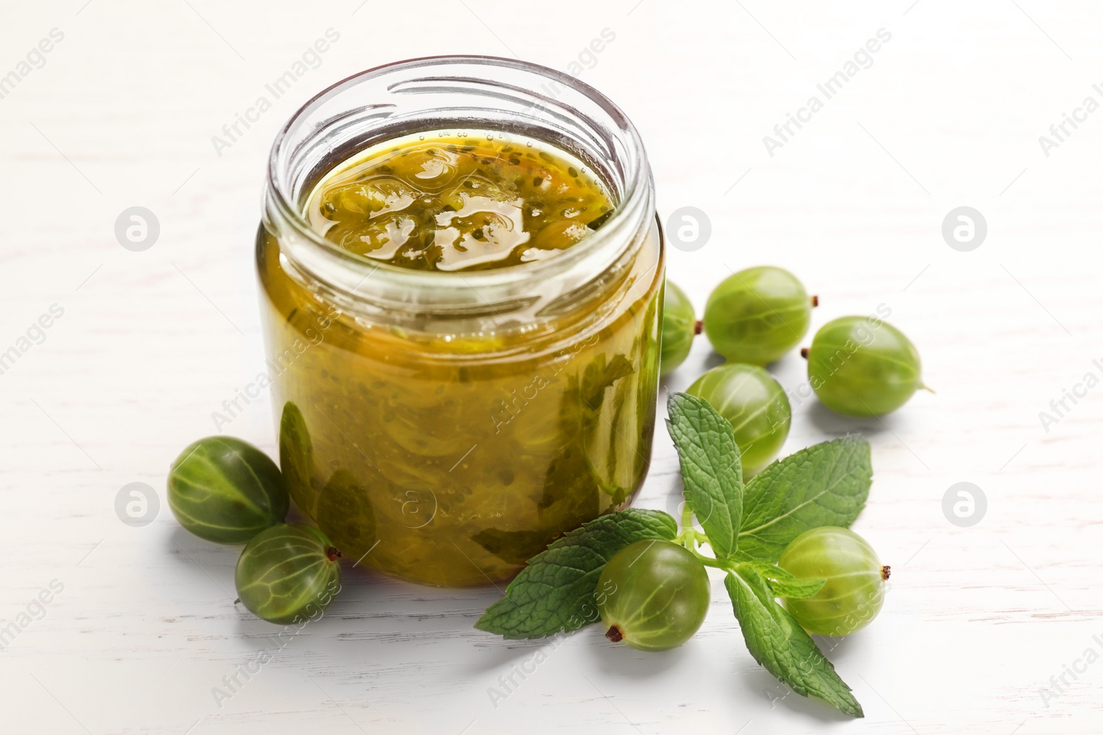 Photo of Jar of delicious gooseberry jam and fresh berries on white wooden table, closeup