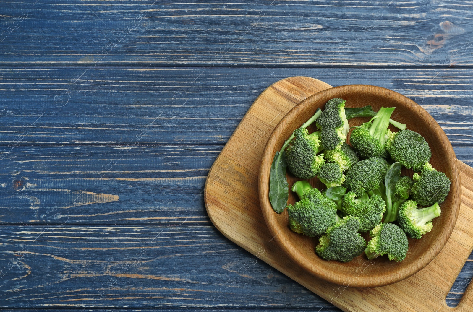 Photo of Bowl of fresh broccoli on blue wooden table, top view with space for text