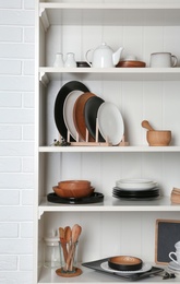 Photo of White shelving unit with set of dishware near brick wall