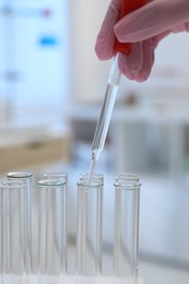 Laboratory analysis. Woman dripping liquid into test tubes indoors, closeup