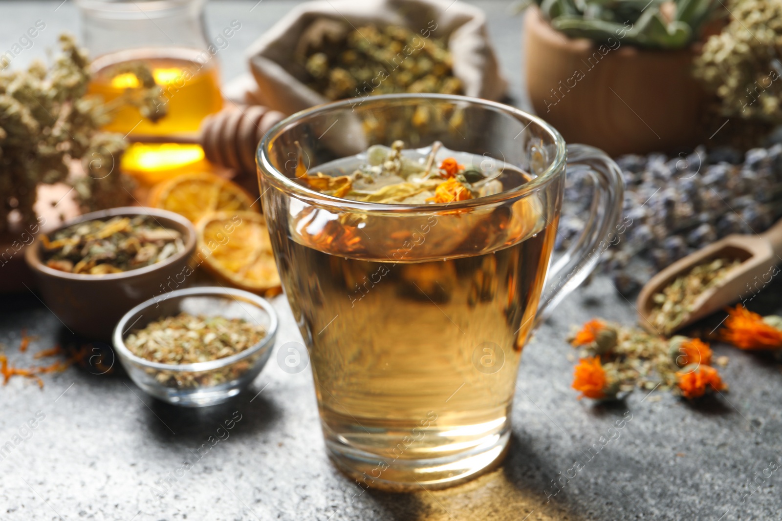 Photo of Freshly brewed tea and dried herbs on grey table, closeup