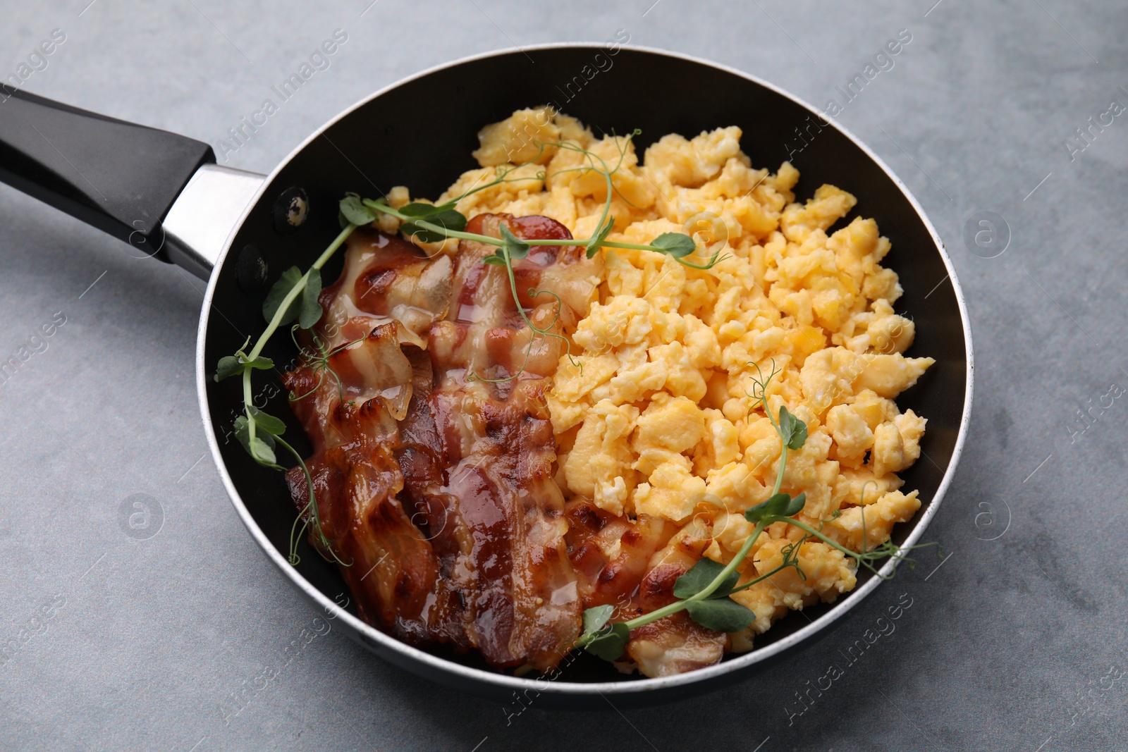 Photo of Delicious scrambled eggs with bacon in frying pan on grey table