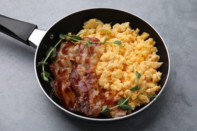 Delicious scrambled eggs with bacon in frying pan on grey table