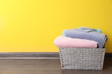 Photo of Basket with clean laundry on floor near yellow wall, space for text