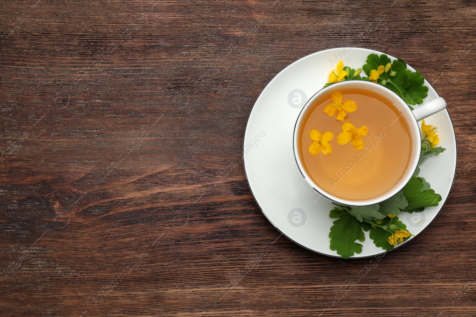 Photo of Cup of aromatic celandine tea and flowers on wooden table, top view. Space for text