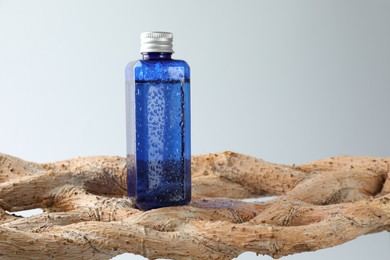 Photo of Bottle of cosmetic product on wooden branch against light grey background, space for text