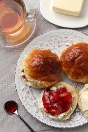 Photo of Freshly baked soda water scones with cranberry jam, butter and cup of tea on table, flat lay