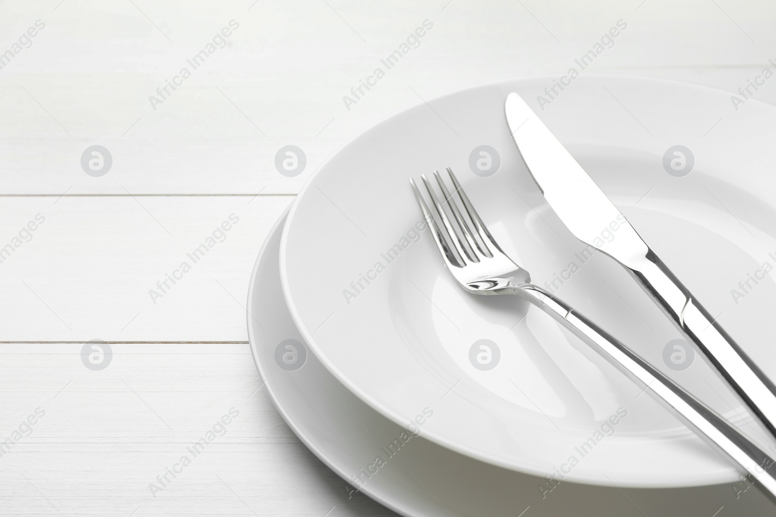 Photo of Clean plates, fork and knife on white wooden table, closeup. Space for text