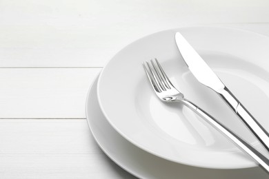 Photo of Clean plates, fork and knife on white wooden table, closeup. Space for text