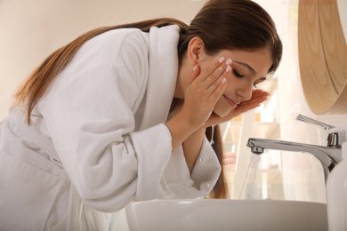 Beautiful teenage girl washing face with water in bathroom