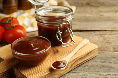 Photo of Tasty barbeque sauce in bowl, jar and spoon on wooden table, closeup. Space for text