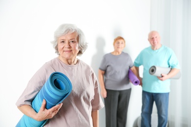 Photo of Elderly woman with yoga mat indoors. Space for text