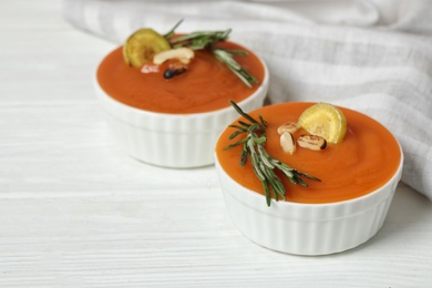 Photo of Tasty puree with baked carrot slices, nuts and rosemary on white wooden table, closeup