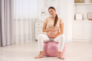 Photo of Pregnant woman sitting on fitness ball at home. Doing yoga