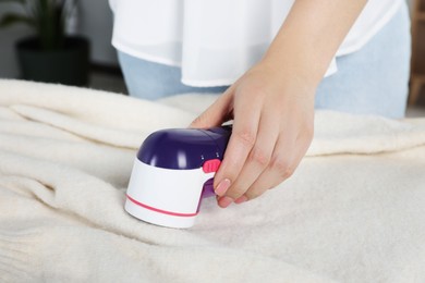 Woman cleaning clothes with fabric shaver indoors, closeup