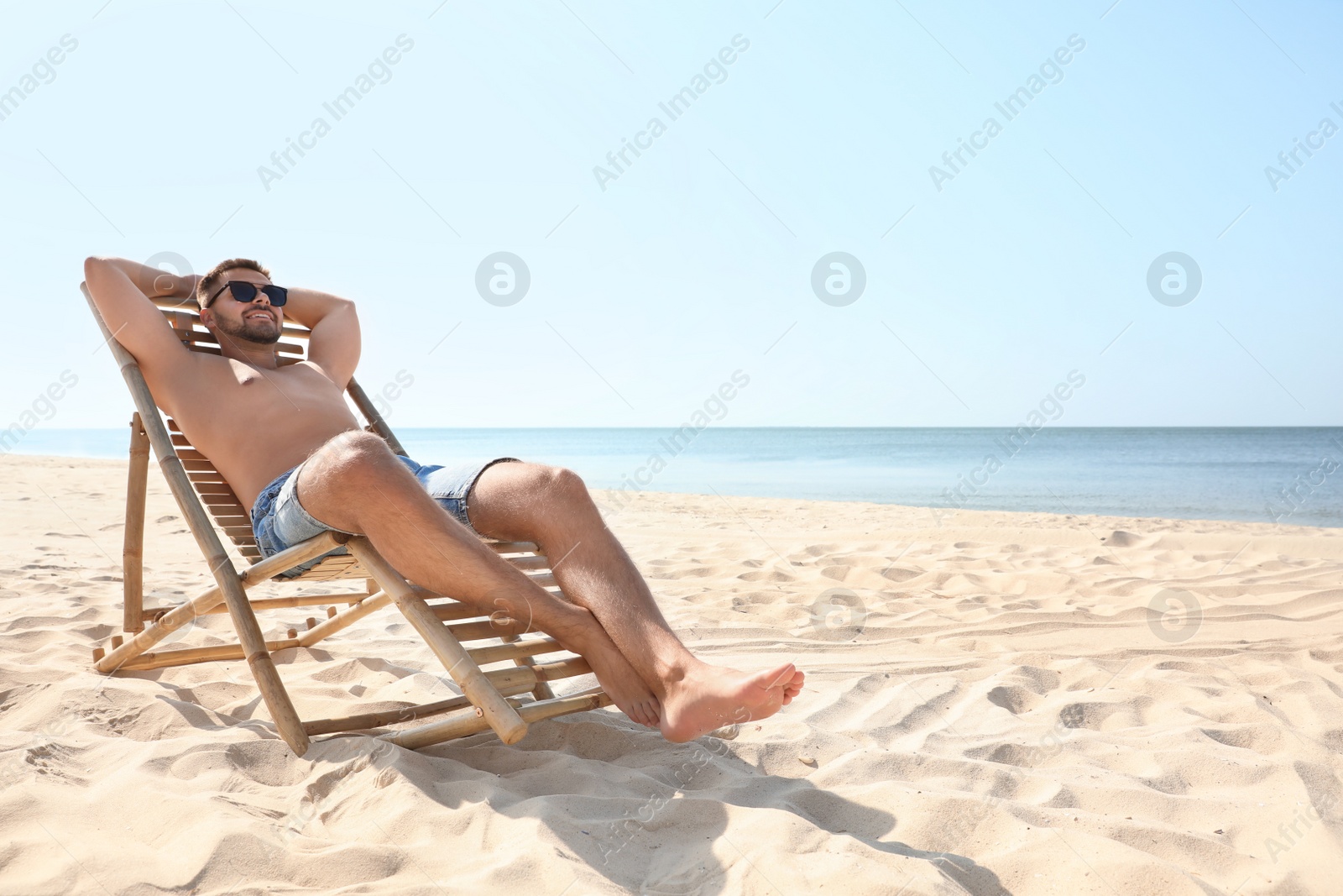 Photo of Young man relaxing in deck chair on sandy beach