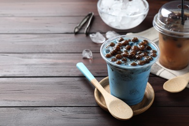 Photo of Tasty blue milk bubble tea and spoon on brown wooden table. Space for text