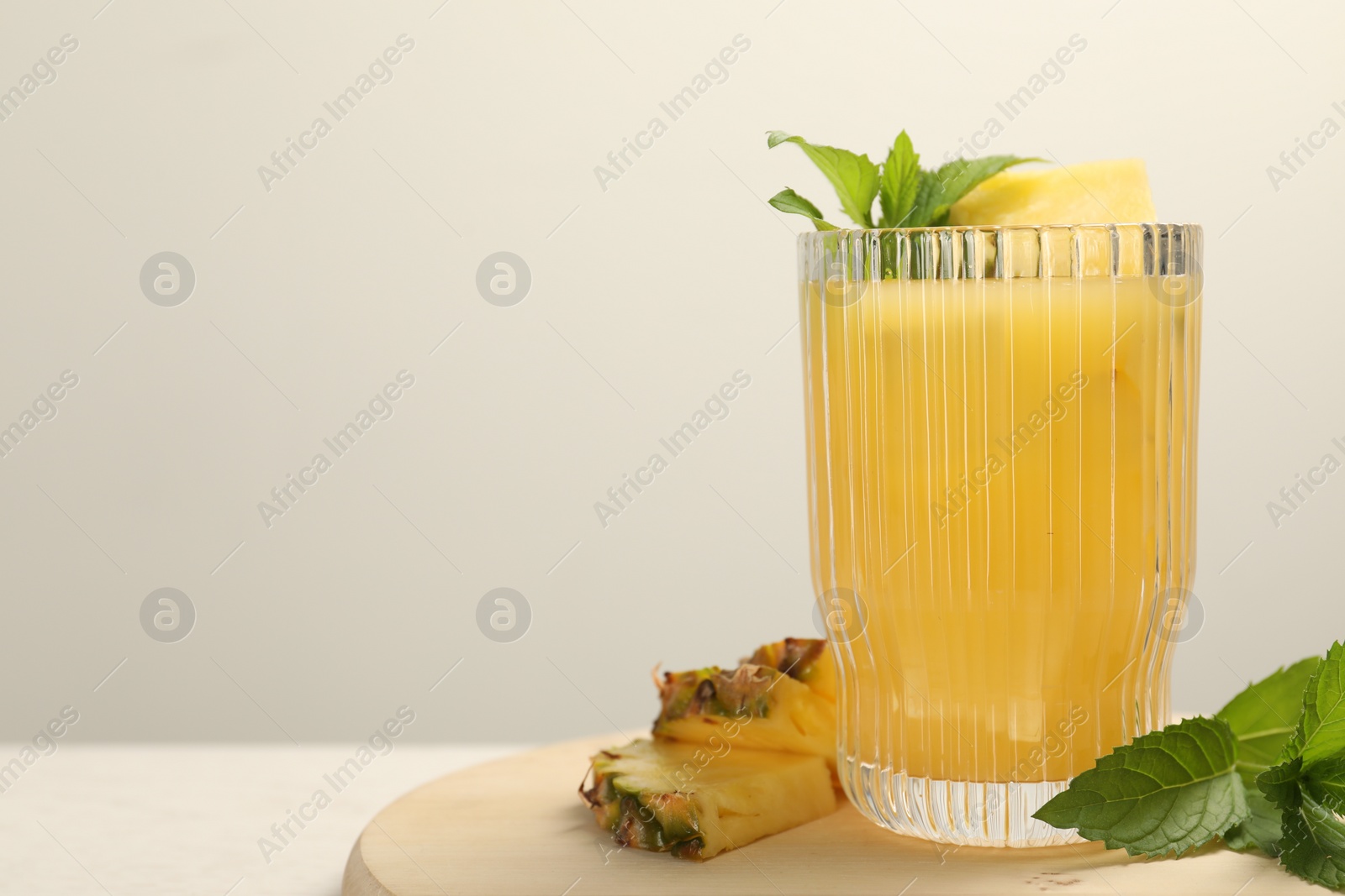 Photo of Glass of tasty pineapple cocktail, mint and sliced fruit on wooden board, closeup. Space for text