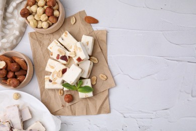 Photo of Pieces of delicious nutty nougat, hazelnuts and almonds on white textured table, flat lay. Space for text