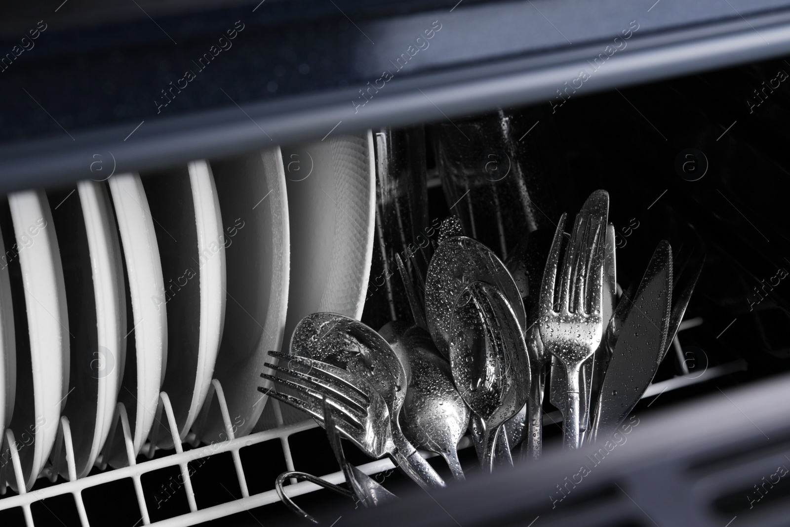 Photo of Clean wet plates and cutlery in dishwasher, closeup