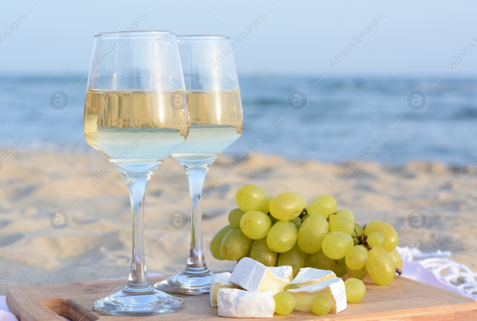 Photo of Glasses with white wine and snacks for beach picnic on sandy seashore