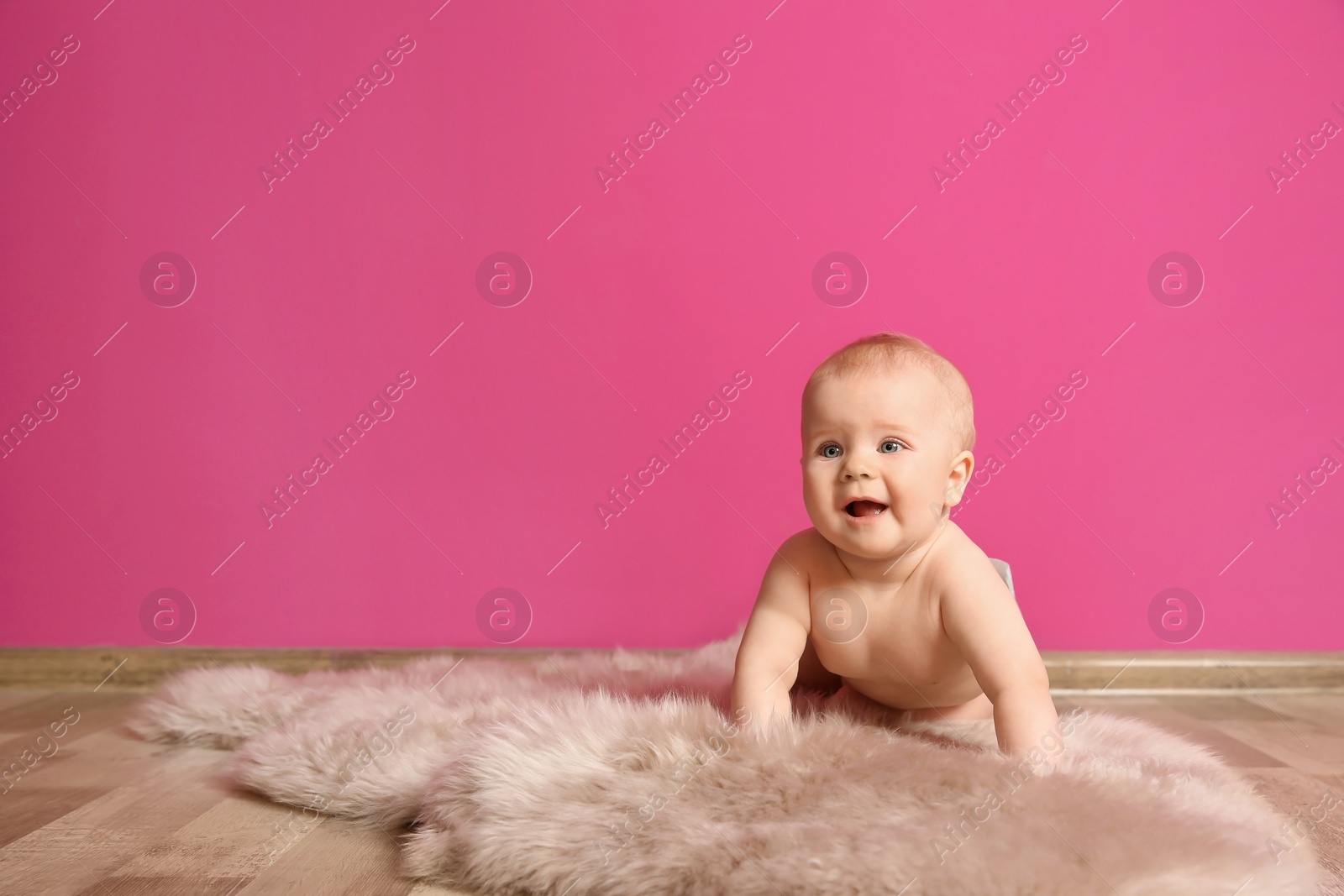 Photo of Cute little baby on fluffy rug near color wall