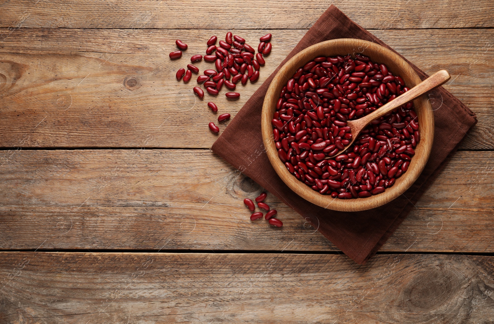 Photo of Raw red kidney beans with bowl, spoon and napkin on wooden table, flat lay. Space for text