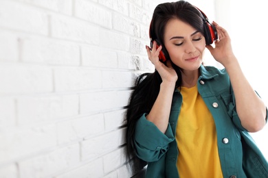 Portrait of beautiful woman listening to music with headphones near brick wall. Space for text