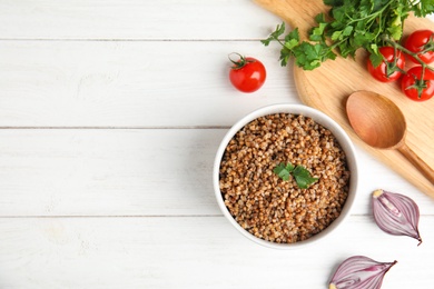 Photo of Flat lay composition with bowl of buckwheat porridge served on white wooden table. Space for text