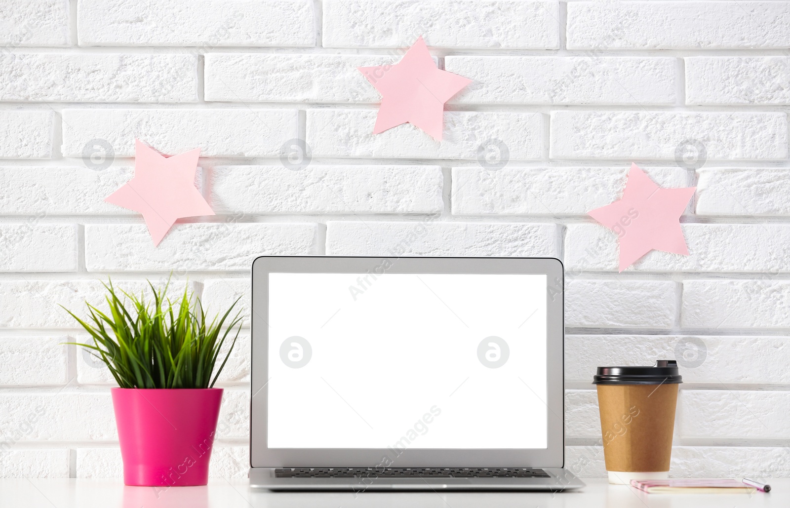 Photo of Modern laptop on desk near brick wall, space for design. Home workplace