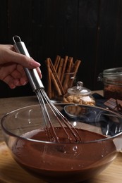 Woman mixing delicious chocolate cream with whisk at table, closeup