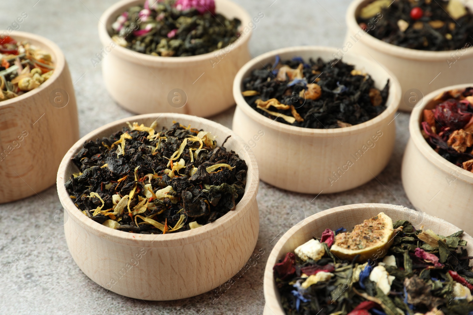 Photo of Different kinds of dry herbal tea in wooden bowls on light grey table