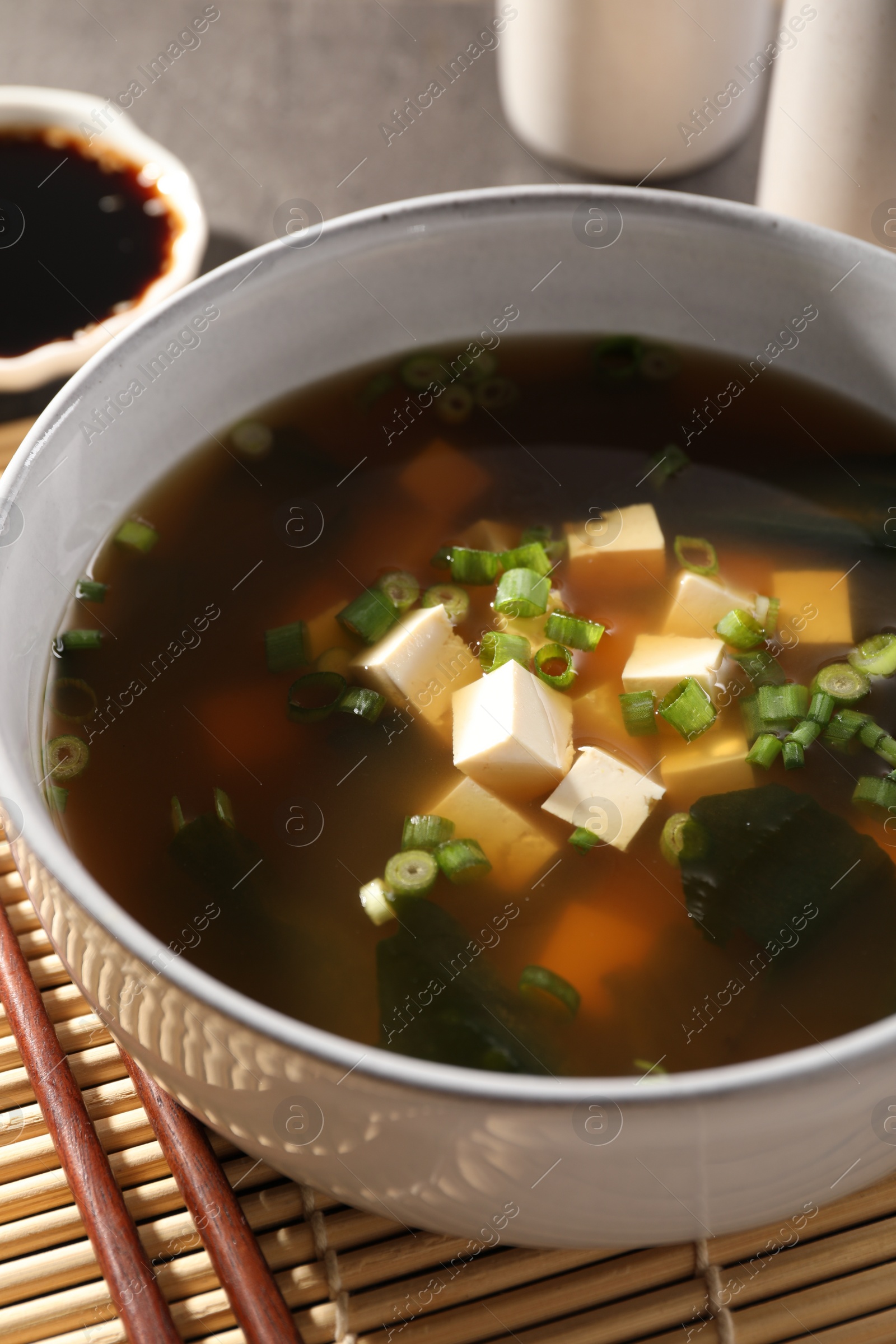 Photo of Bowl of delicious miso soup with tofu and chopsticks on bamboo mat, closeup