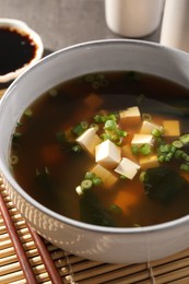 Bowl of delicious miso soup with tofu and chopsticks on bamboo mat, closeup