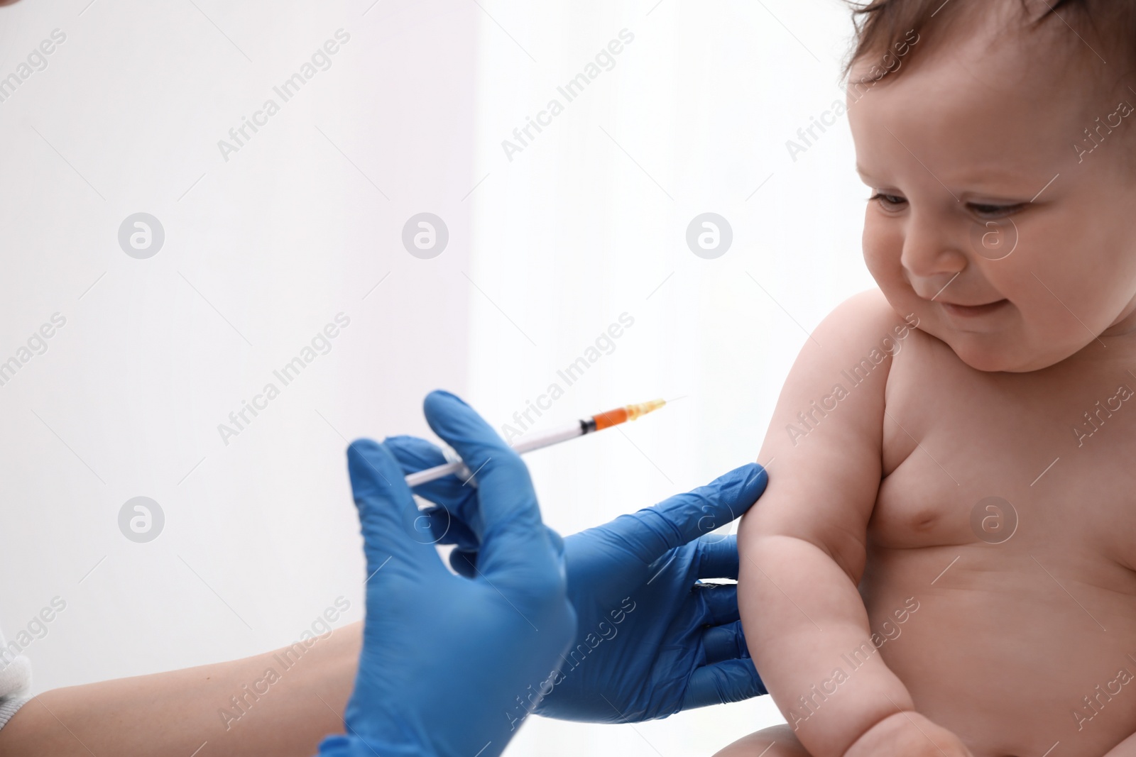 Photo of Doctor vaccinating baby against light background. Health care