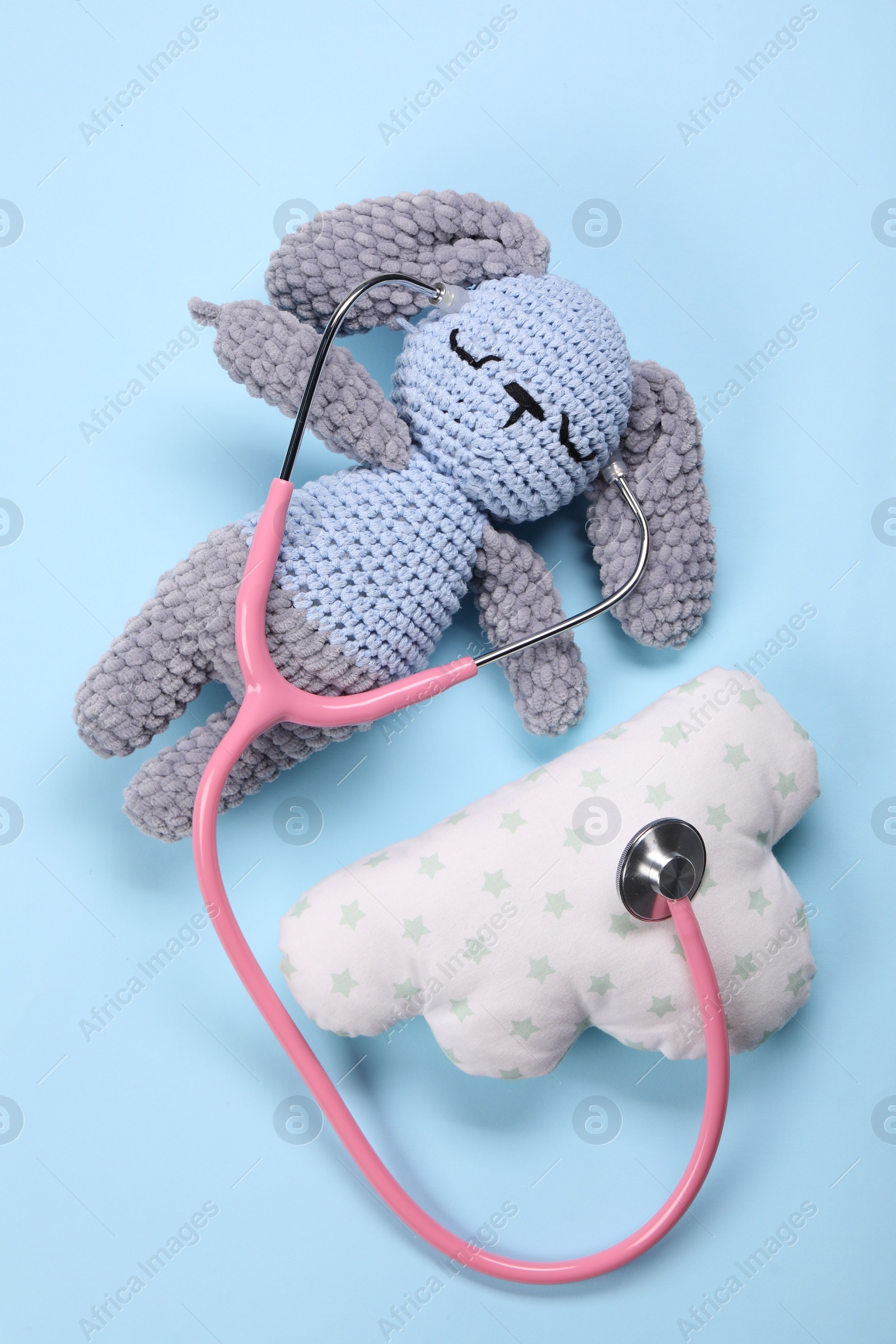 Photo of Toy bunny, pillow and stethoscope on light blue background, flat lay