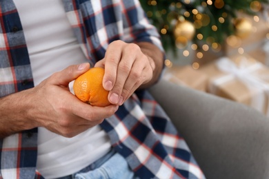 Man with tangerine near Christmas tree, closeup