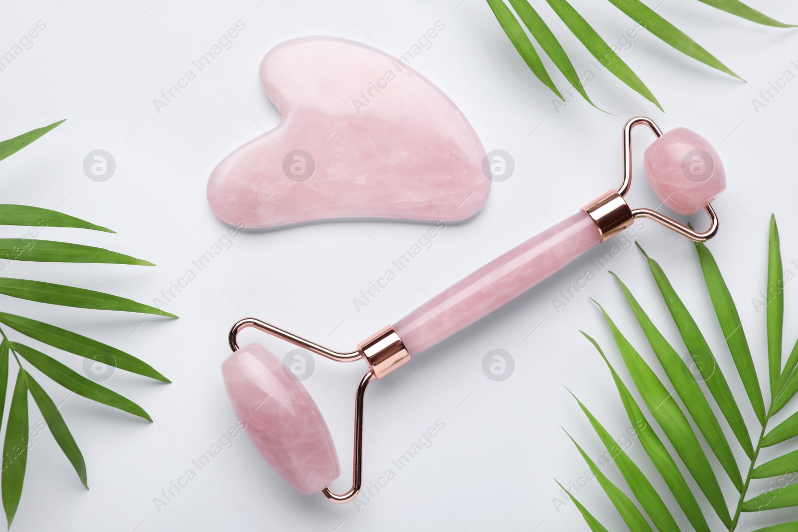 Photo of Gua sha stone, face roller and green leaves on white background, flat lay