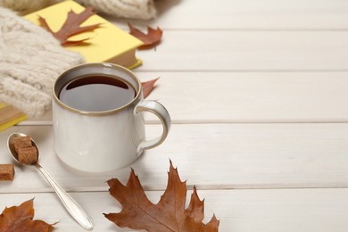 Photo of Cup of hot tea, sweater and autumn leaves on white wooden table, space for text