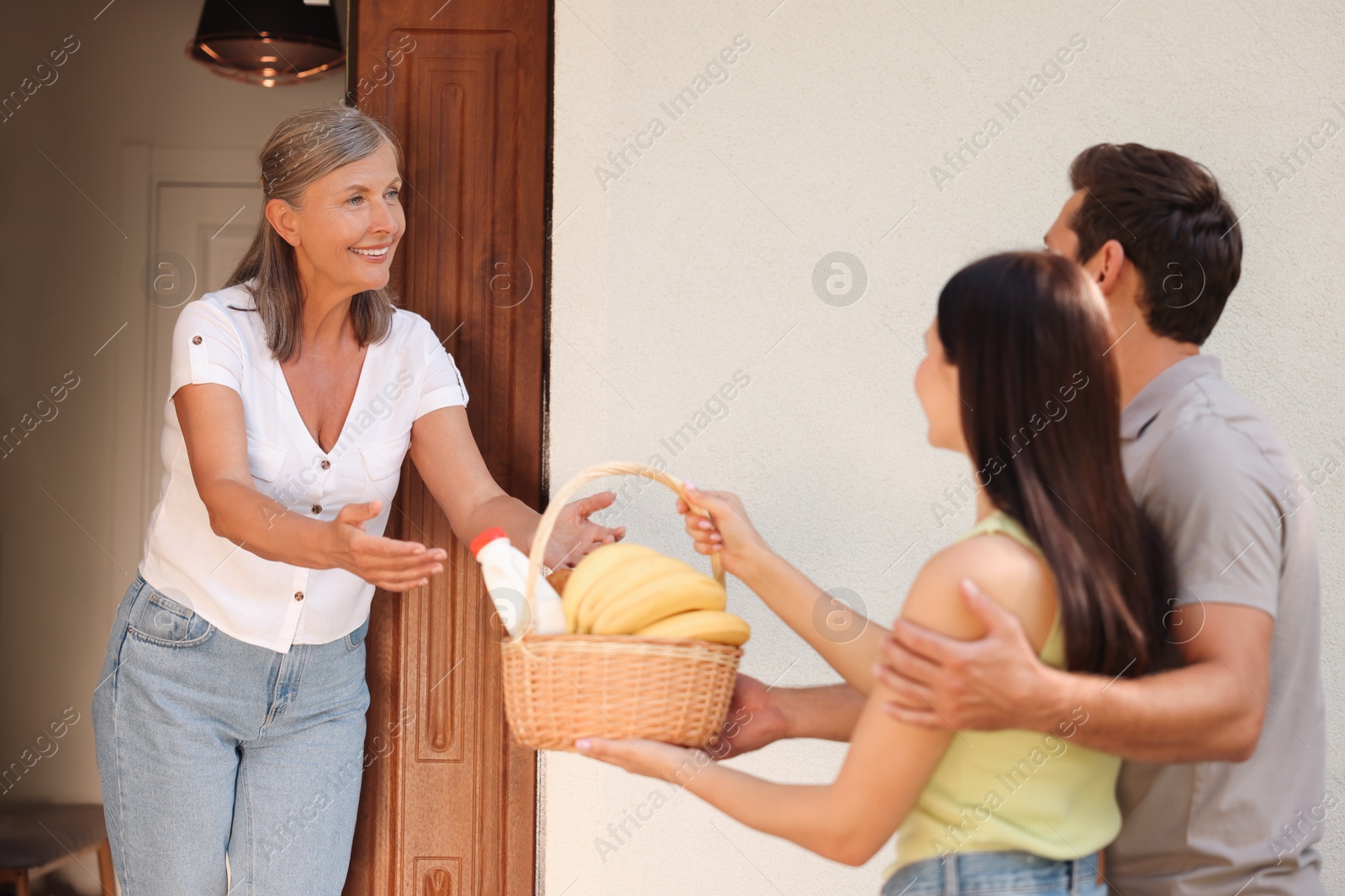 Photo of Friendly relationship with neighbours. Young couple with wicker basket of products treating senior woman outdoors