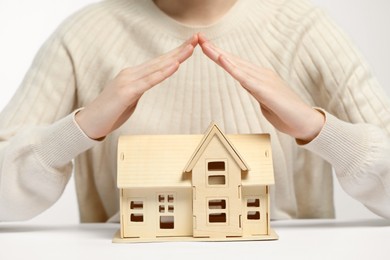 Home security concept. Woman covering house model at white table, closeup