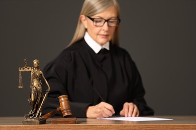 Photo of Judge working with document indoors, selective focus. Mallet and figure of Lady Justice on wooden table