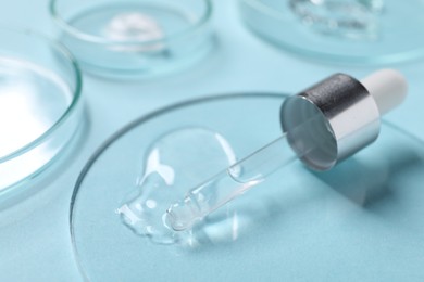 Petri dish with cosmetic serum and pipette on light blue background, closeup