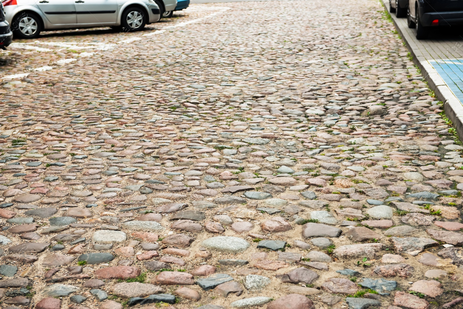 Photo of View on old stone sidewal near cars. Footpath covering