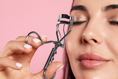 Photo of Young woman using eyelash curler on light pink background, closeup