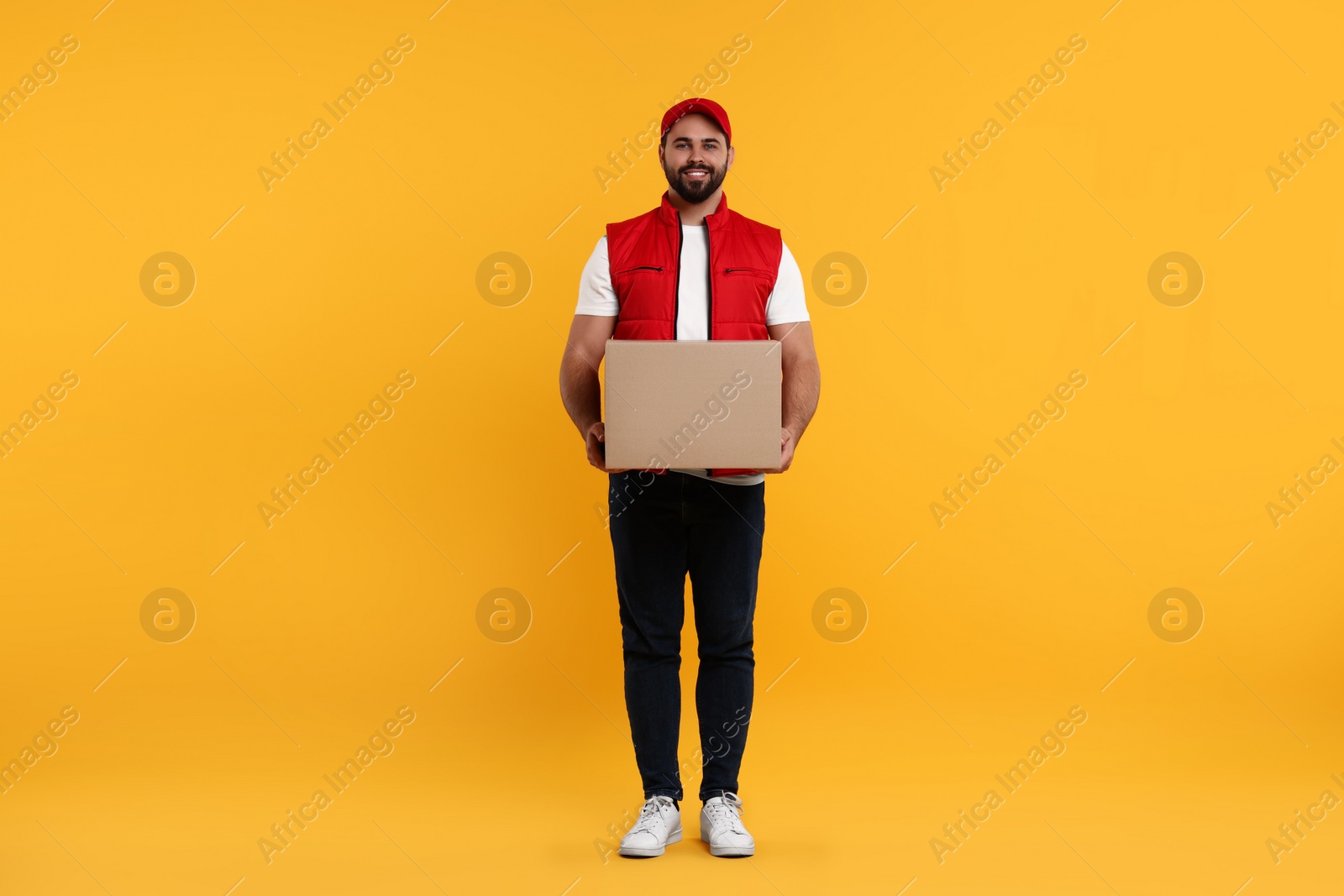 Photo of Happy young courier with parcel on orange background