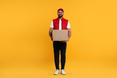 Happy young courier with parcel on orange background