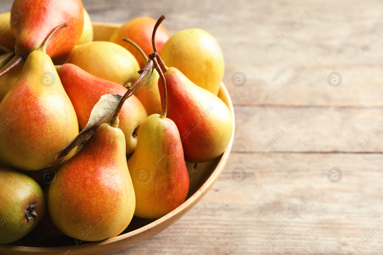 Photo of Bowl with ripe pears on wooden background, closeup. Space for text