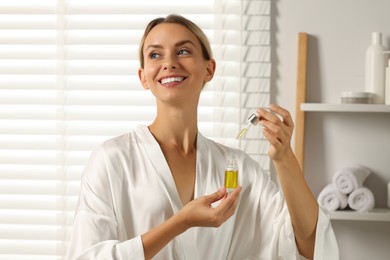 Beautiful woman with cosmetic serum in her hands in bathroom